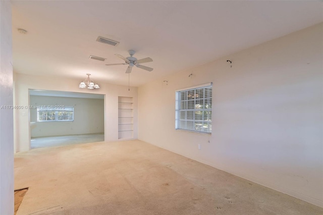 carpeted empty room with built in shelves and ceiling fan with notable chandelier