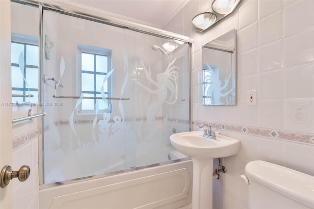 bathroom featuring ornamental molding, tile walls, shower / bath combination with glass door, and toilet