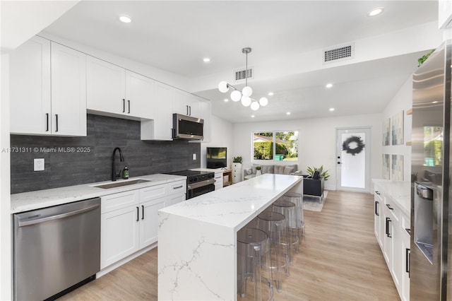 kitchen featuring appliances with stainless steel finishes, pendant lighting, white cabinetry, sink, and light stone counters