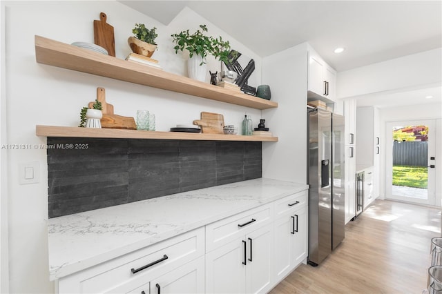 bar with light stone countertops, white cabinets, light hardwood / wood-style floors, and stainless steel fridge with ice dispenser