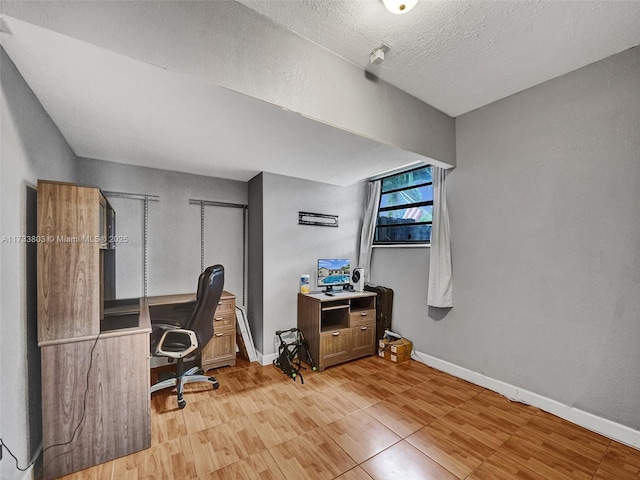 home office with light hardwood / wood-style floors and a textured ceiling