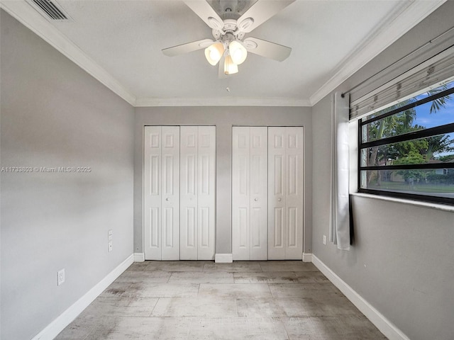 unfurnished bedroom featuring ceiling fan, ornamental molding, light wood-type flooring, and two closets