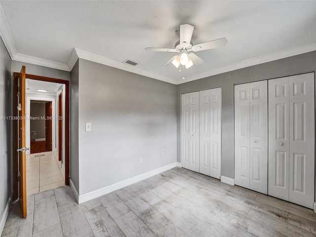 unfurnished bedroom with multiple closets, ceiling fan, crown molding, and light wood-type flooring