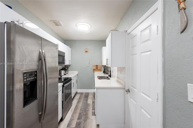 kitchen with sink, light hardwood / wood-style flooring, appliances with stainless steel finishes, white cabinetry, and a textured ceiling