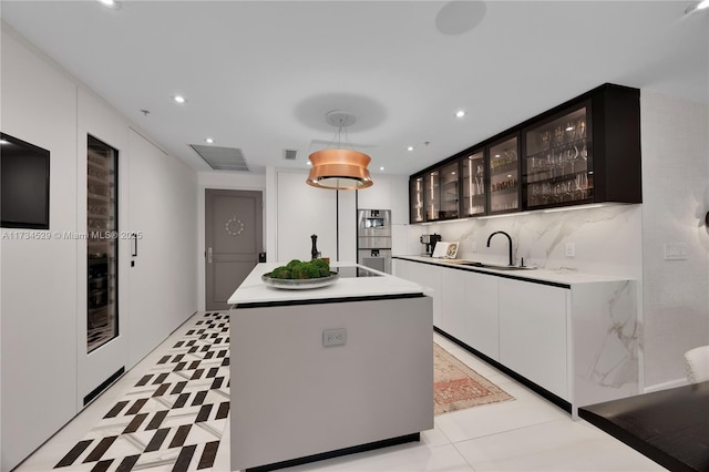 kitchen with sink, white cabinetry, hanging light fixtures, double wall oven, and an island with sink