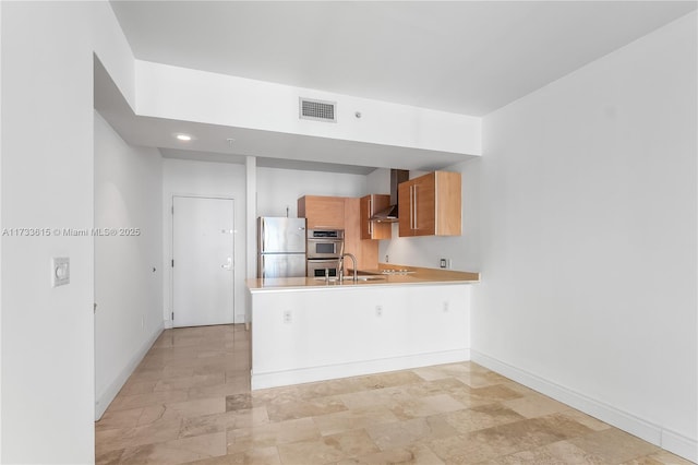 kitchen featuring stainless steel appliances, kitchen peninsula, sink, and wall chimney range hood