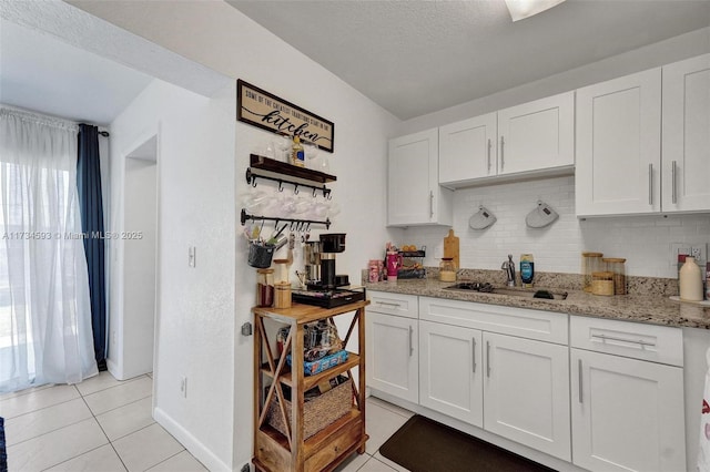 kitchen featuring sink, light tile patterned floors, white cabinets, and backsplash