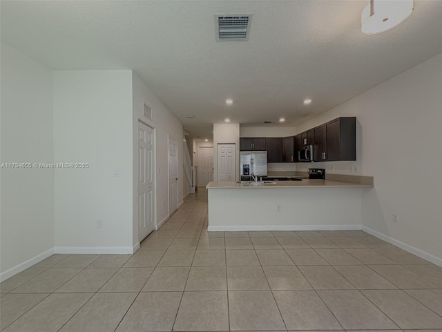 kitchen with a textured ceiling, dark brown cabinets, light tile patterned floors, appliances with stainless steel finishes, and kitchen peninsula