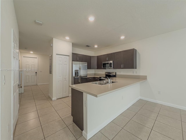 kitchen with dark brown cabinetry, sink, light tile patterned floors, kitchen peninsula, and stainless steel appliances