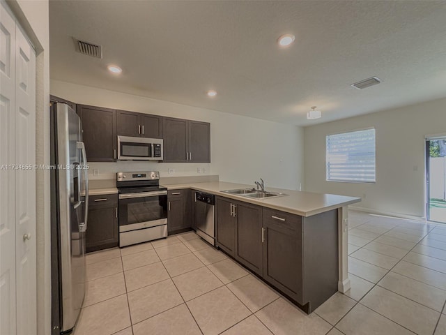 kitchen with sink, light tile patterned floors, appliances with stainless steel finishes, dark brown cabinets, and kitchen peninsula