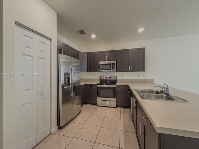 kitchen with dark brown cabinetry, sink, a textured ceiling, light tile patterned floors, and appliances with stainless steel finishes