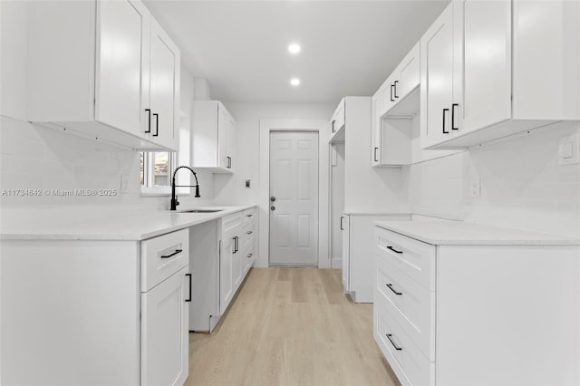 kitchen featuring white cabinetry, sink, decorative backsplash, and light hardwood / wood-style flooring