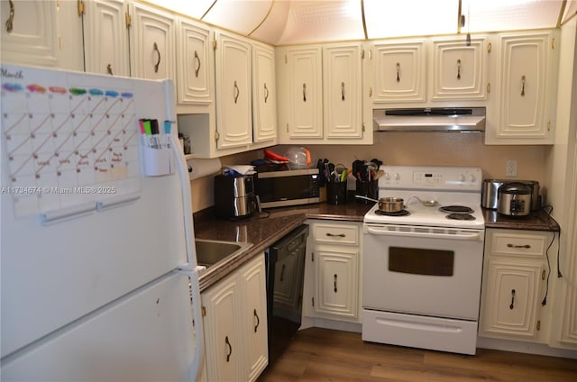 kitchen featuring under cabinet range hood, white appliances, a sink, wood finished floors, and dark countertops