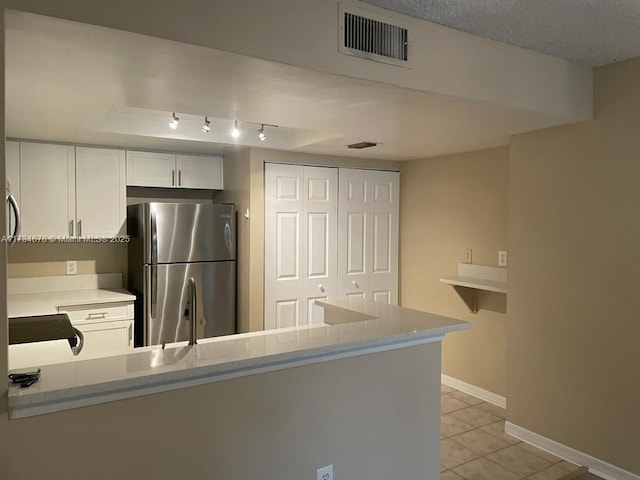 kitchen featuring white cabinetry, light tile patterned floors, stainless steel fridge, and kitchen peninsula