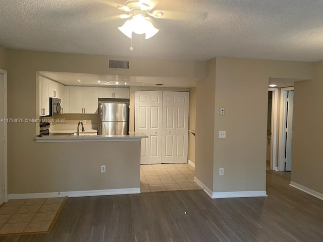 kitchen featuring wood-type flooring, a textured ceiling, appliances with stainless steel finishes, kitchen peninsula, and white cabinets