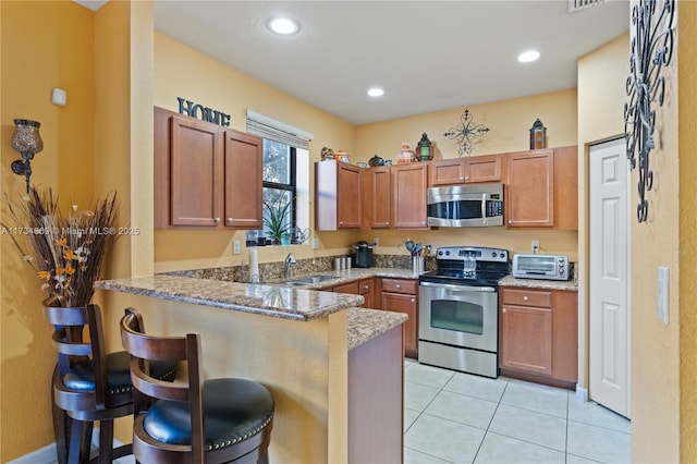 kitchen with light tile patterned flooring, appliances with stainless steel finishes, a kitchen breakfast bar, kitchen peninsula, and stone counters