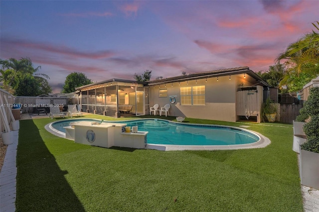 pool at dusk featuring a hot tub and a lawn