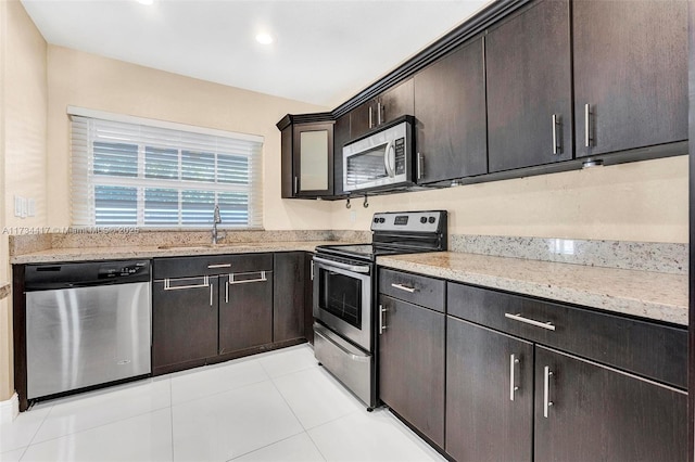 kitchen featuring stainless steel appliances, dark brown cabinets, sink, and light stone counters