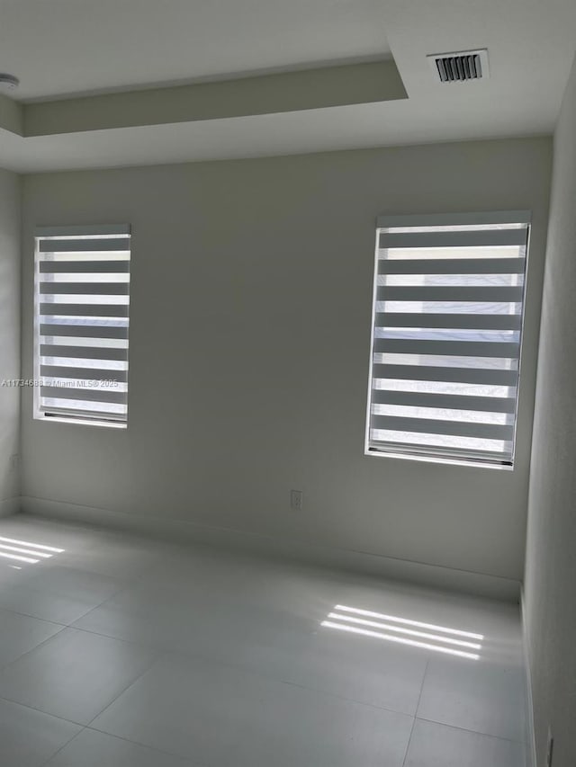 tiled empty room featuring a healthy amount of sunlight and a tray ceiling