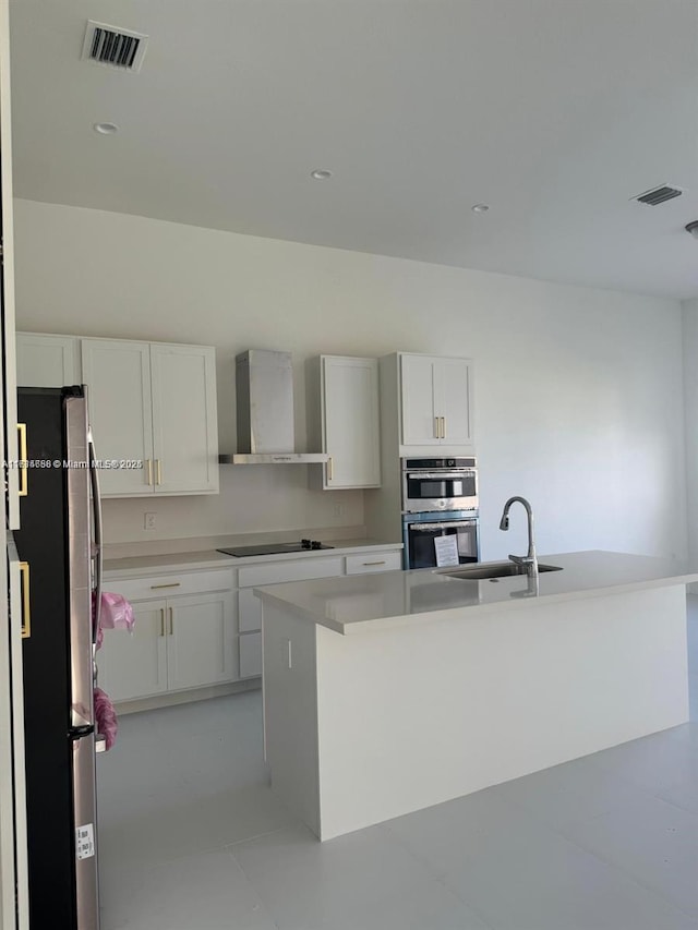 kitchen featuring wall chimney exhaust hood, stainless steel appliances, a kitchen island with sink, and white cabinets