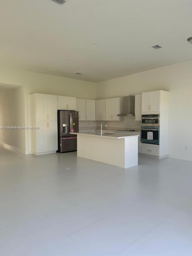 kitchen with sink, white cabinetry, stainless steel appliances, a kitchen island with sink, and wall chimney range hood