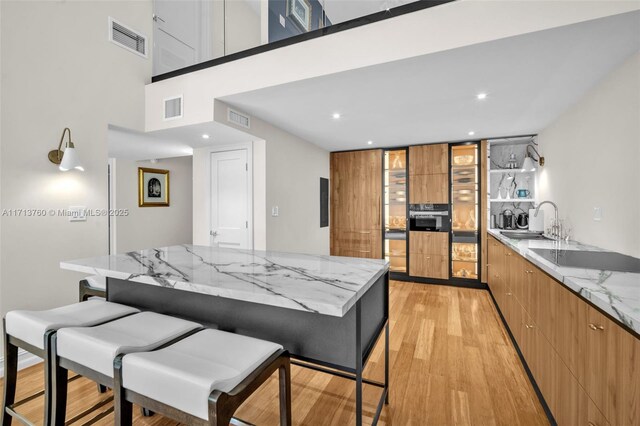 kitchen featuring sink, a breakfast bar area, light stone counters, black electric stovetop, and light hardwood / wood-style floors