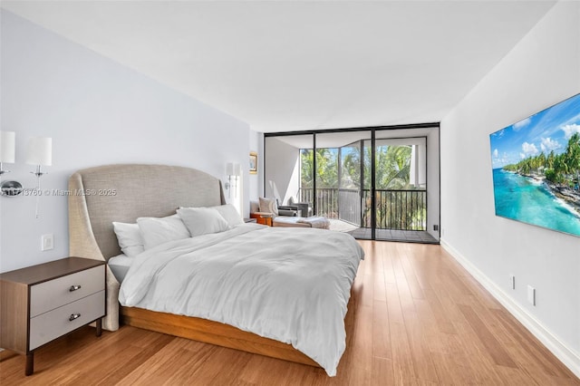 bedroom featuring access to exterior, baseboards, light wood finished floors, and expansive windows