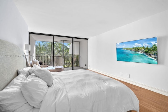 bedroom featuring baseboards, wood finished floors, floor to ceiling windows, and access to outside