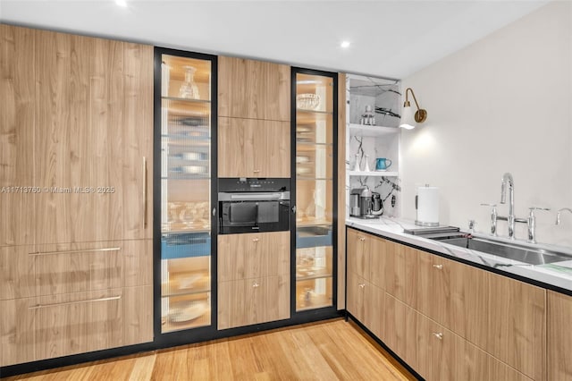 kitchen featuring light wood finished floors, modern cabinets, light brown cabinetry, and a sink