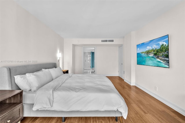 bedroom featuring ensuite bath, wood finished floors, visible vents, and baseboards