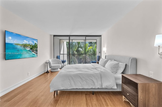 bedroom with access to outside, baseboards, light wood finished floors, and expansive windows