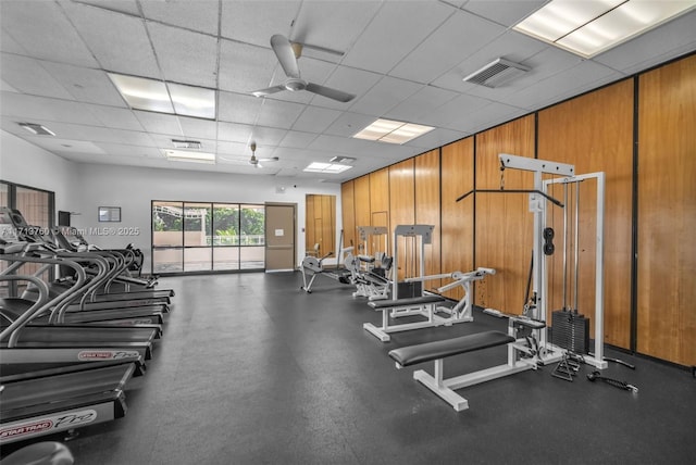 exercise room featuring a paneled ceiling, visible vents, and wood walls