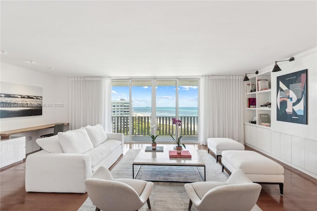 living room featuring wood-type flooring, built in features, floor to ceiling windows, and a water view