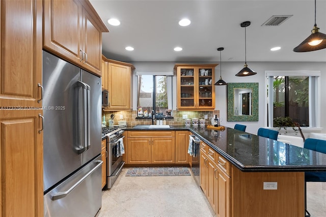 kitchen with sink, dark stone countertops, high quality appliances, decorative backsplash, and decorative light fixtures