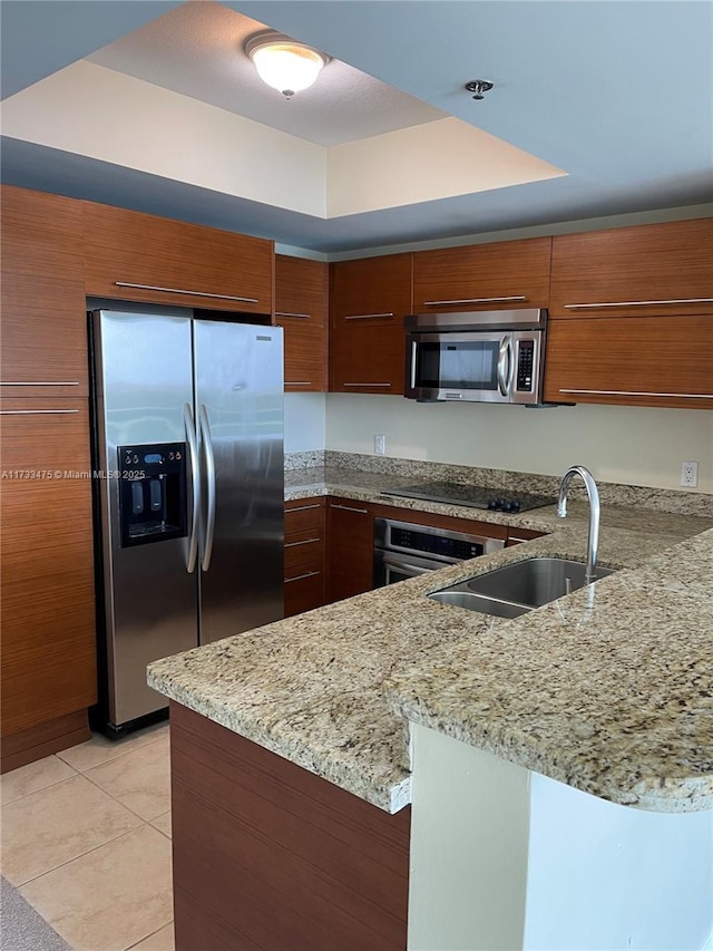 kitchen with light tile patterned floors, a tray ceiling, kitchen peninsula, and appliances with stainless steel finishes