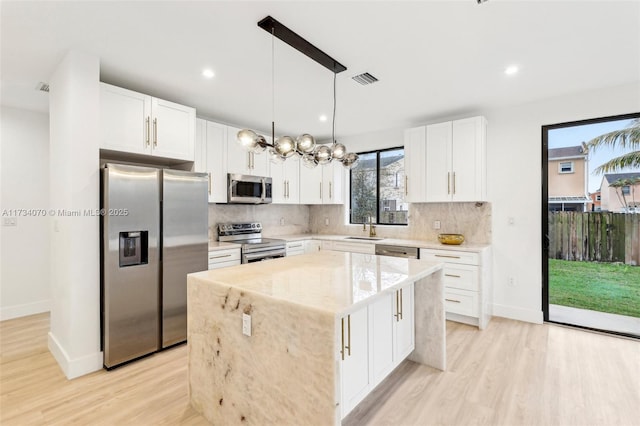 kitchen featuring a kitchen island, appliances with stainless steel finishes, hanging light fixtures, and white cabinets