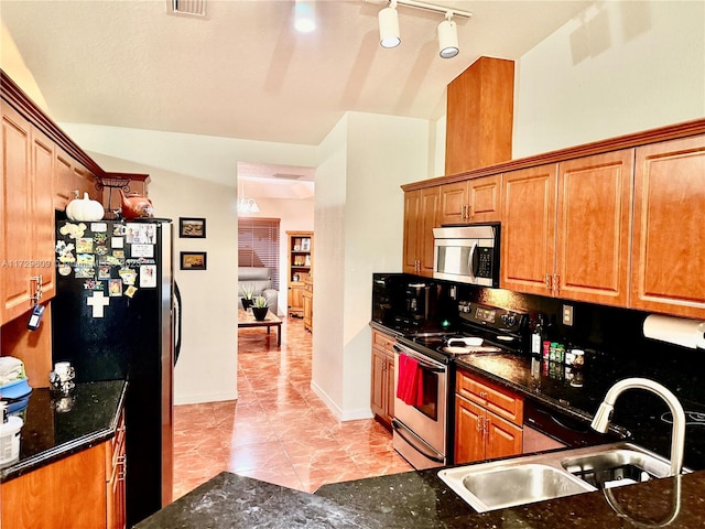 kitchen with stainless steel appliances, dark stone countertops, sink, and light tile patterned floors