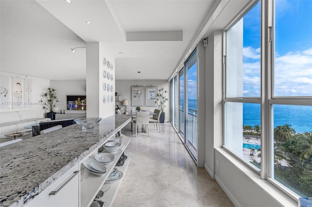 kitchen with light stone counters, hanging light fixtures, white cabinets, and a water view