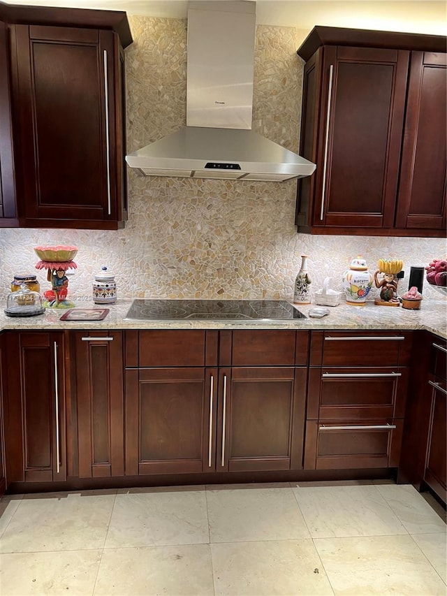 kitchen featuring tasteful backsplash, wall chimney range hood, light stone counters, and black electric stovetop