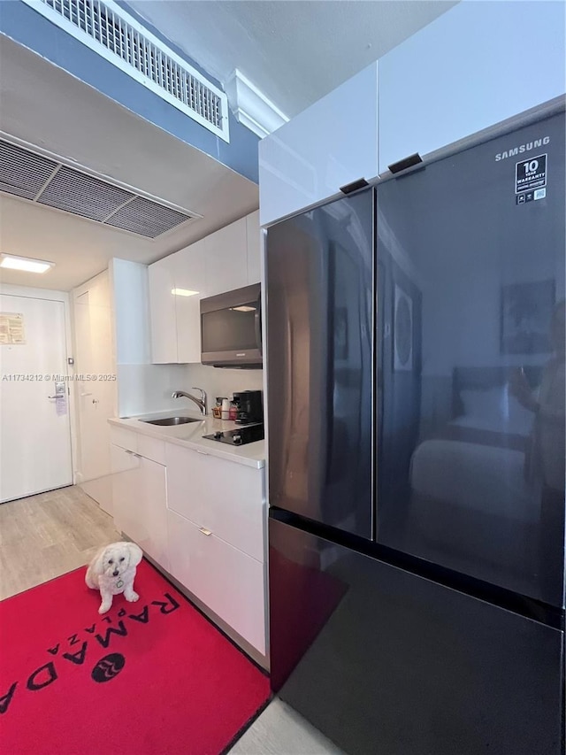 kitchen featuring sink, light hardwood / wood-style flooring, stainless steel refrigerator, black electric stovetop, and white cabinets