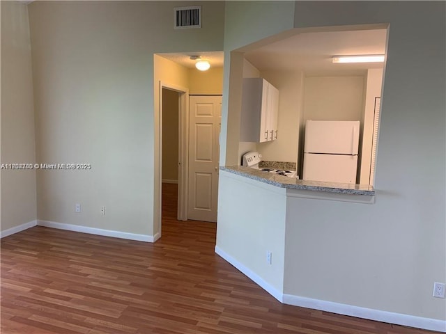 kitchen featuring white cabinetry, white fridge, hardwood / wood-style floors, and stove