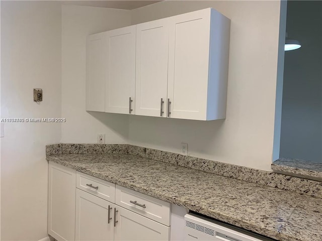 kitchen featuring dishwashing machine, light stone countertops, and white cabinets