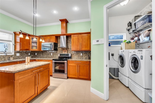 kitchen with light stone counters, separate washer and dryer, hanging light fixtures, appliances with stainless steel finishes, and wall chimney range hood