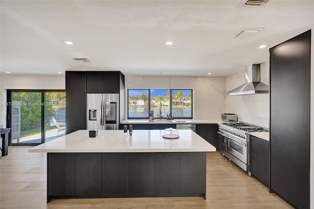 kitchen featuring wall chimney exhaust hood, sink, a center island with sink, light hardwood / wood-style flooring, and appliances with stainless steel finishes