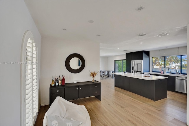 kitchen featuring appliances with stainless steel finishes, a center island with sink, and light wood-type flooring