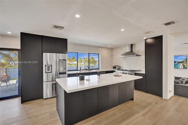 kitchen featuring sink, a center island, stainless steel fridge, light hardwood / wood-style floors, and wall chimney range hood