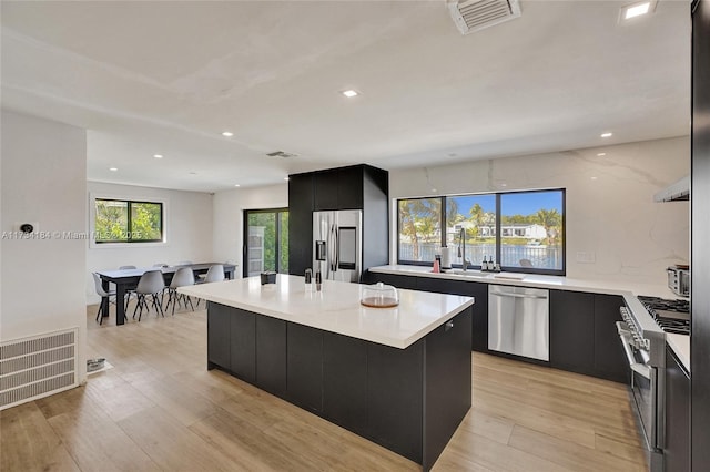 kitchen with sink, appliances with stainless steel finishes, a kitchen island with sink, light hardwood / wood-style floors, and decorative backsplash