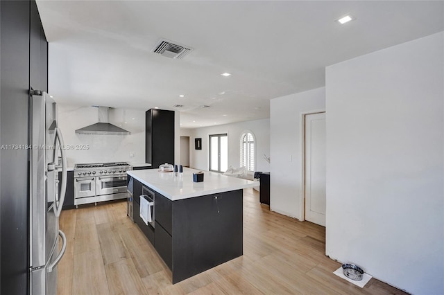 kitchen featuring stainless steel appliances, a center island, wall chimney exhaust hood, and light wood-type flooring