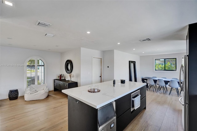 kitchen with plenty of natural light, light hardwood / wood-style floors, a center island, and stainless steel fridge