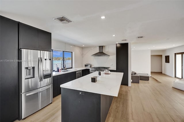 kitchen featuring a kitchen island, sink, stainless steel appliances, wall chimney range hood, and light hardwood / wood-style flooring